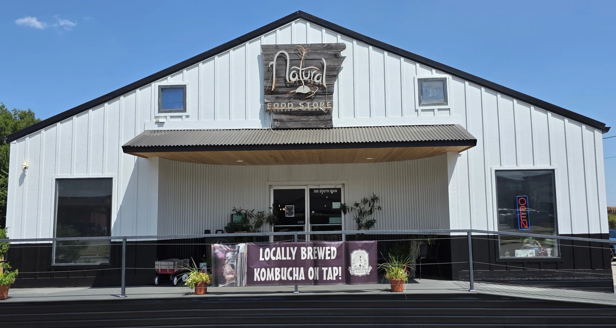 The white barn-style storefront of Natural Food Store on South Main, with a Locally Brewed Kombucha On Tap banner across the porch